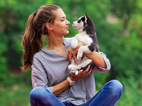 A woman is holding a puppy and they looking at each other.